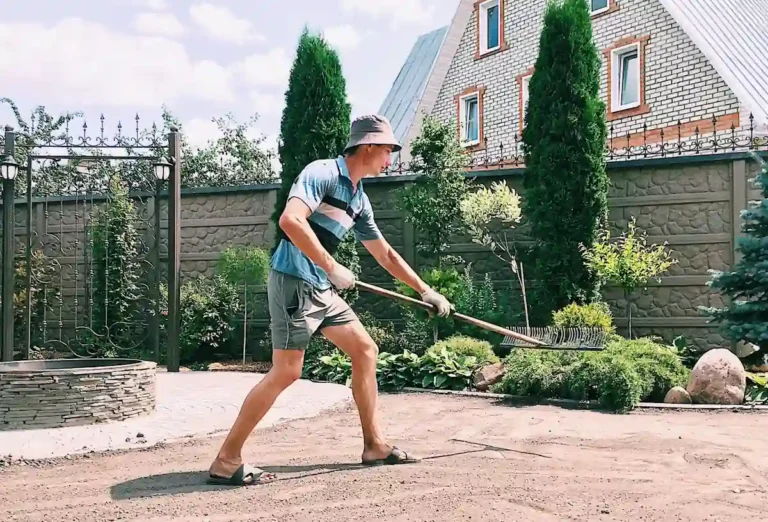 Un homme qui ratisse le sol pour faire une place de parking dans son jardin