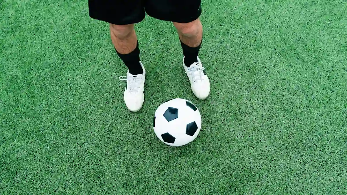 Un homme debout avec un ballon sur un terrain de foot avec un gazon synthétique
